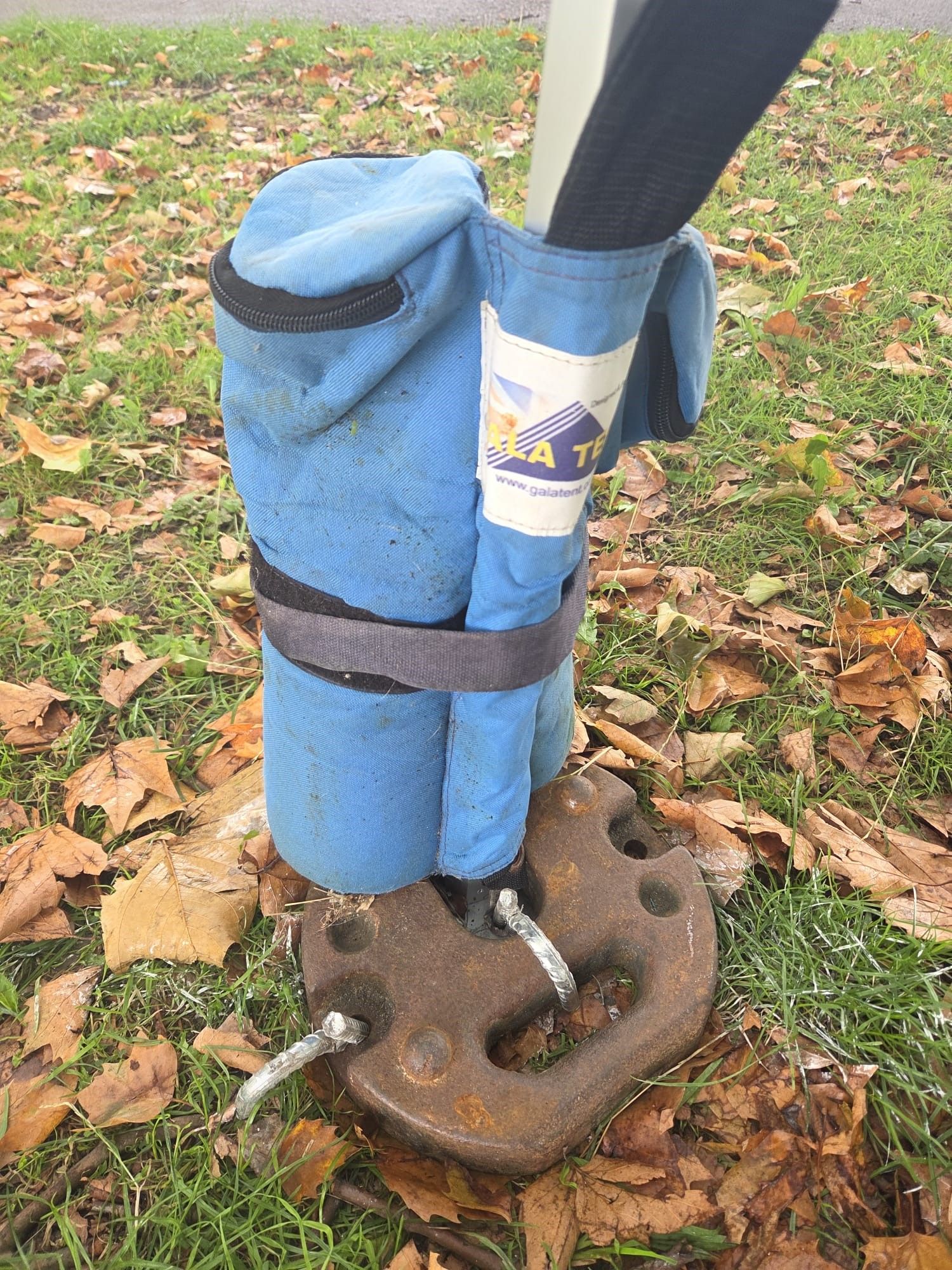 Gala Tent gazebo leg triple-anchored with a leg weight bag, a cast iron weight and heavy duty pegs