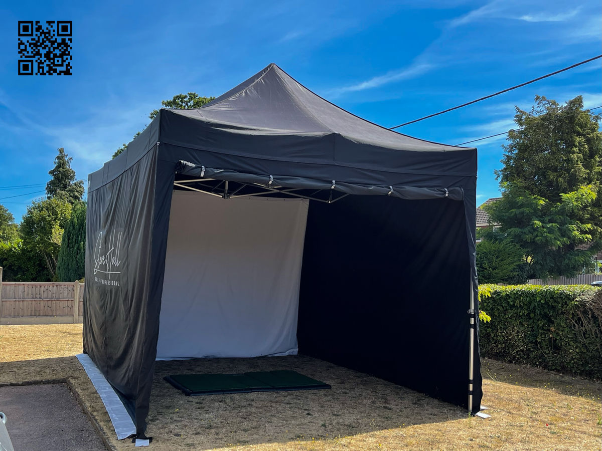 Black Gala Shade Pro 50 gazebo on extension legs, branded for a golf professional, with sidewalls, a white hitting screen and a practice mat inside
