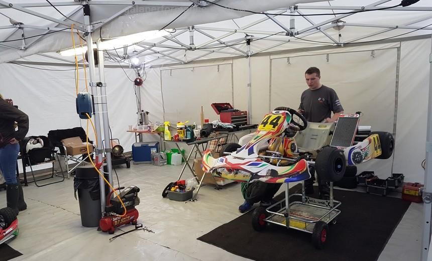 Family working on a cadet kart under an awning between heats