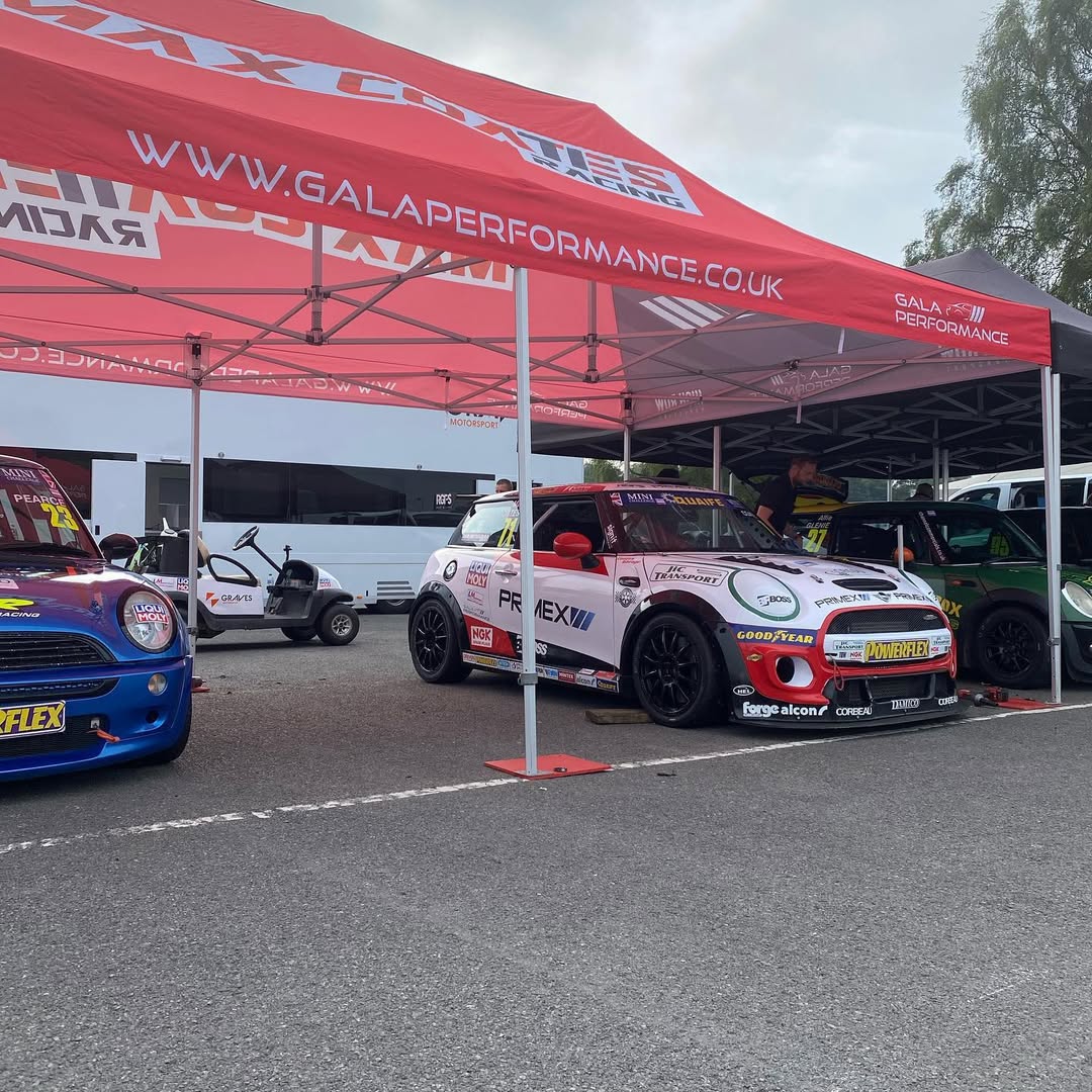 Grass paddock at a hillclimb venue with competition cars and awnings