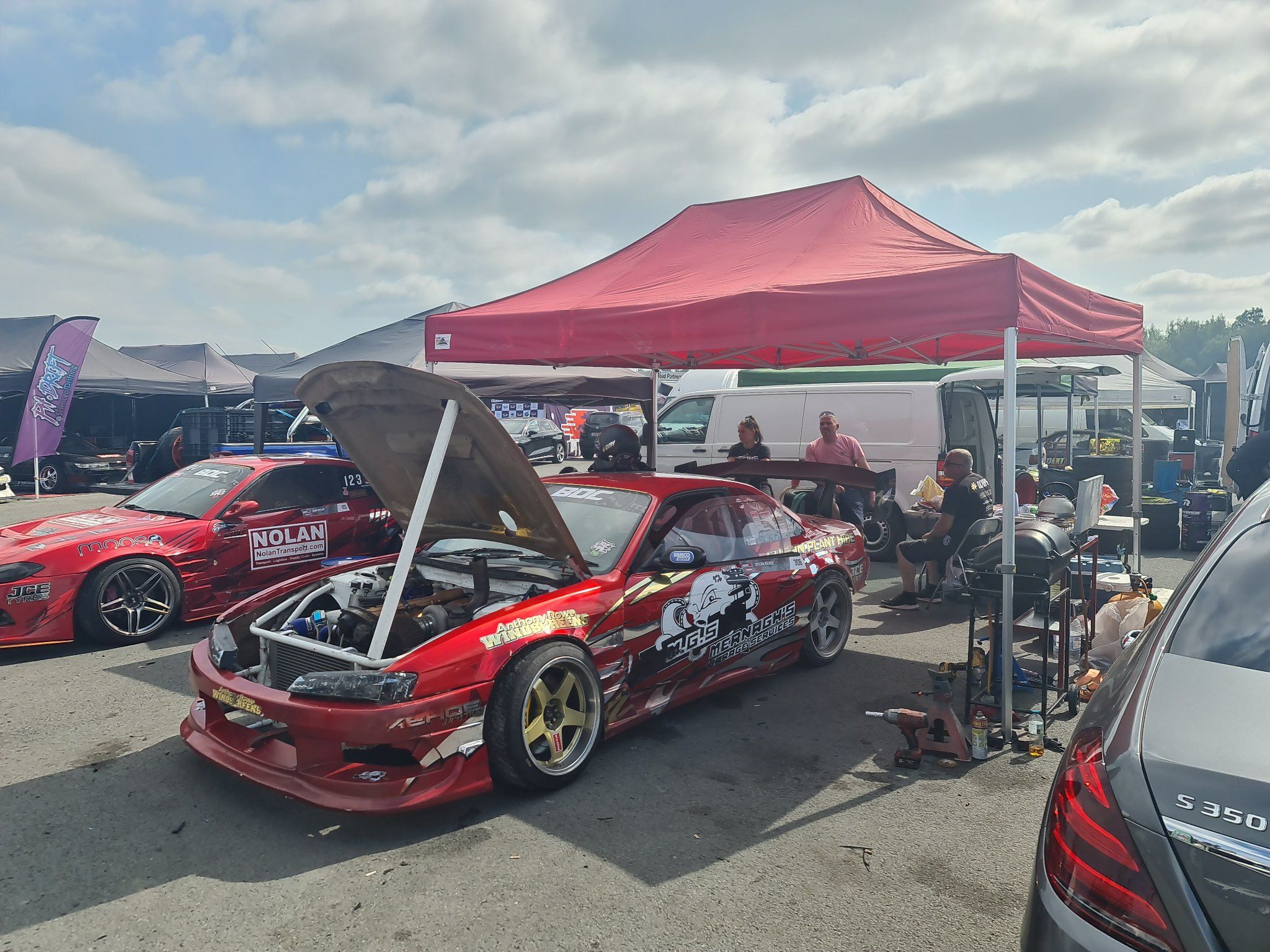 Drift team working on a car under a race awning between sessions
