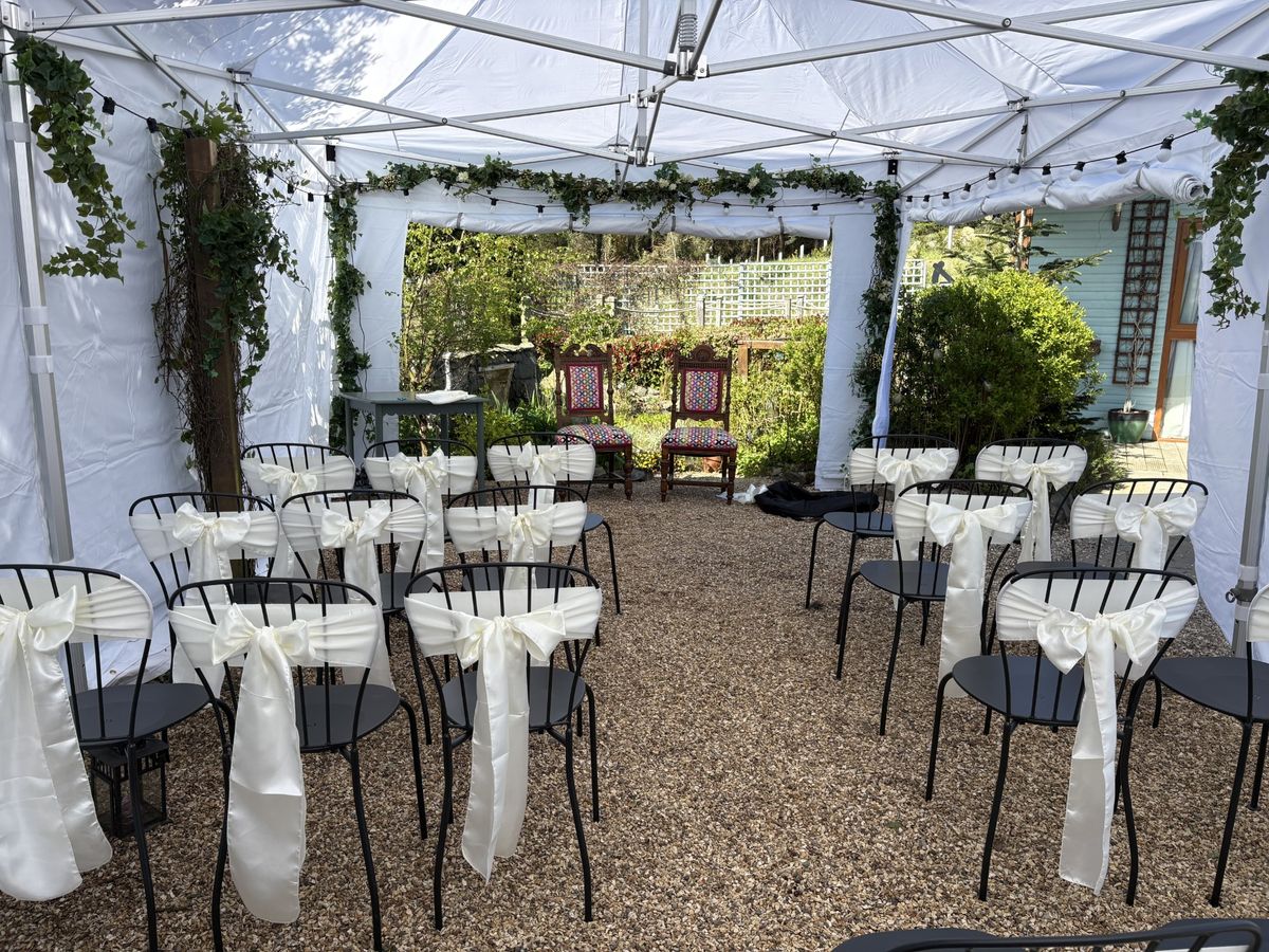 White Gala Tent gazebo with sidewalls set out for a garden wedding ceremony, with rows of chairs tied with ivory sashes and ivy garlands on the frame